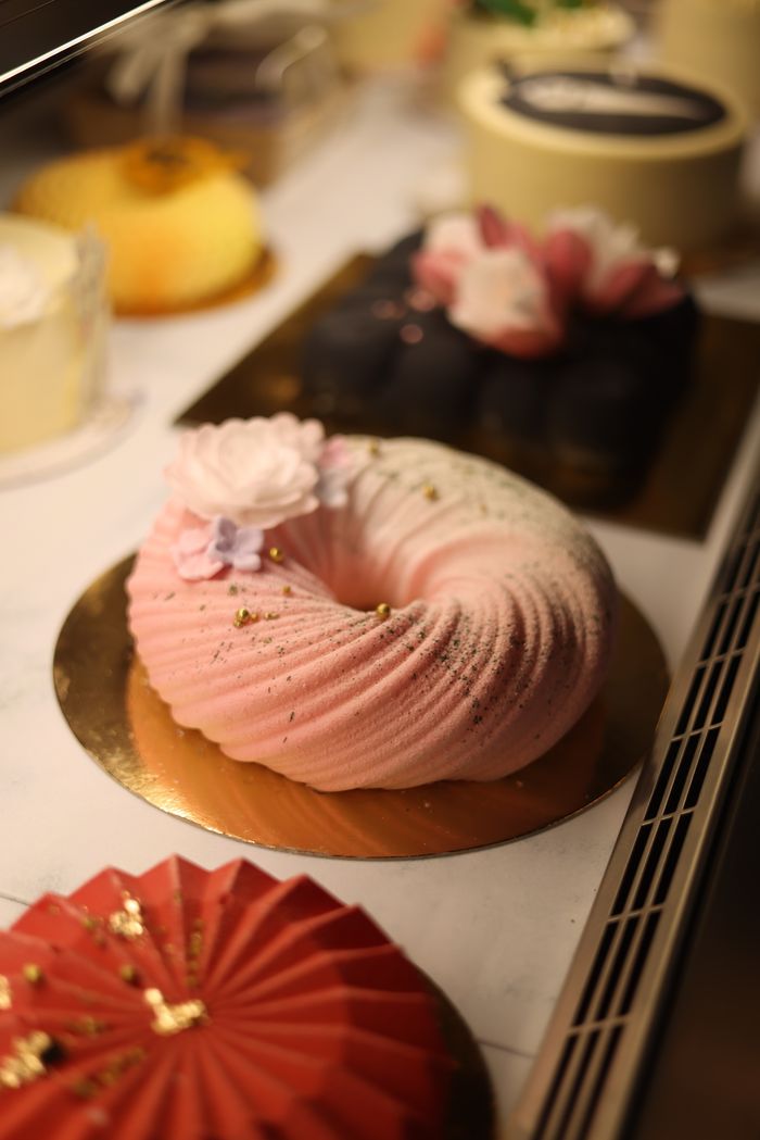 Delicate pink torus-shaped cake adorned with flowers in a bakery showcase. Ideal for dessert lovers.