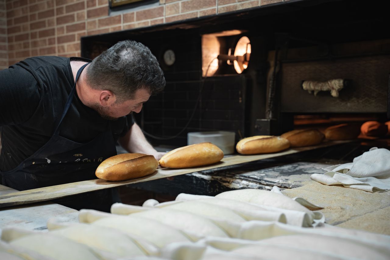 Home An artisan baker placing loaves of bread in a traditional oven.