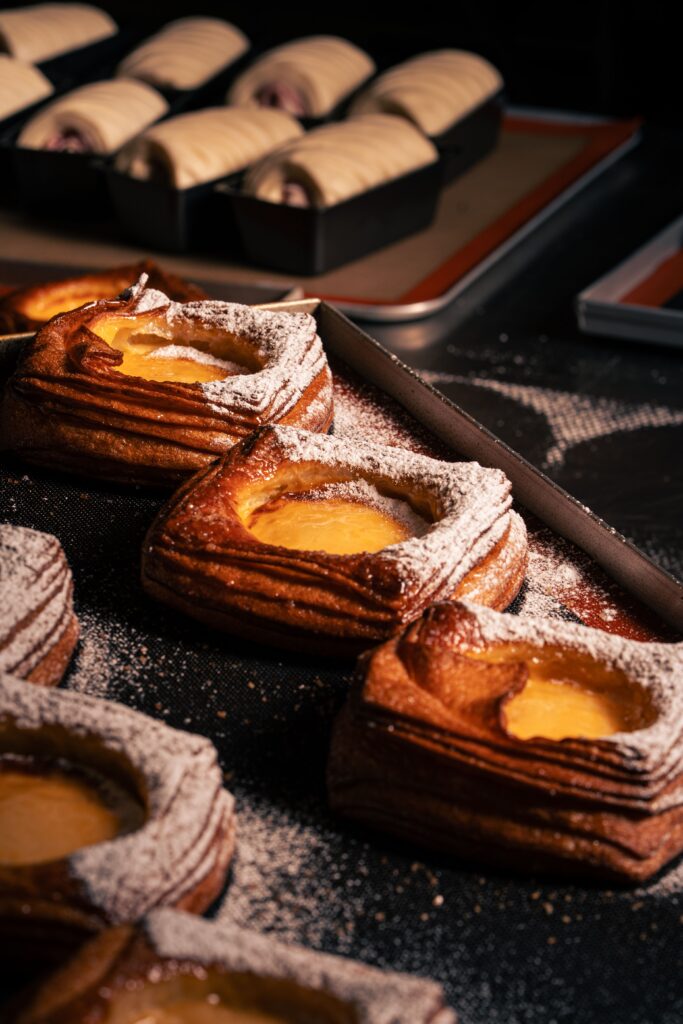 Freshly baked pastries dusted with powdered sugar in a bakery setting, showcasing delicious golden brown crusts.